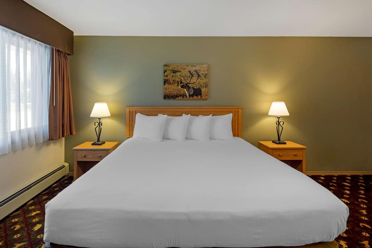 A hotel room with a large bed, two bedside tables with lamps, a window with curtains, and a wall-mounted painting of a deer.