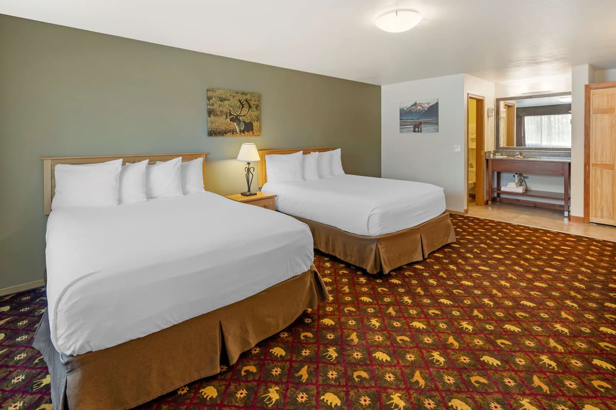 A hotel room with two beds, a nightstand with a lamp, a patterned carpet, and a painting on the wall.