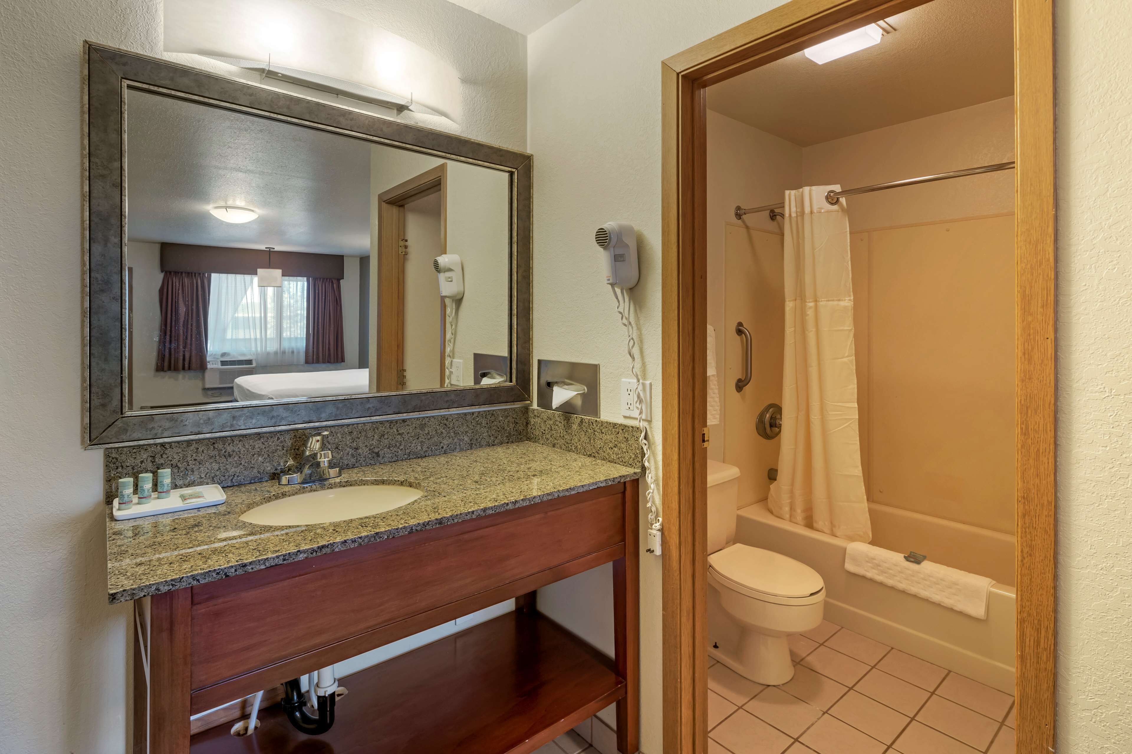 A bathroom with a granite countertop sink, a large mirror, a hair dryer, and a shower with a curtain.