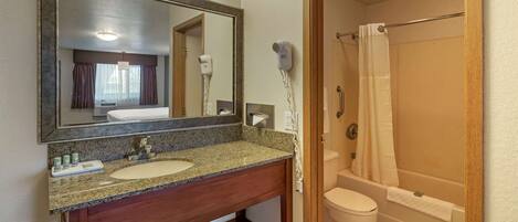 A bathroom with a granite countertop sink, a large mirror, a hair dryer, and a shower with a curtain.