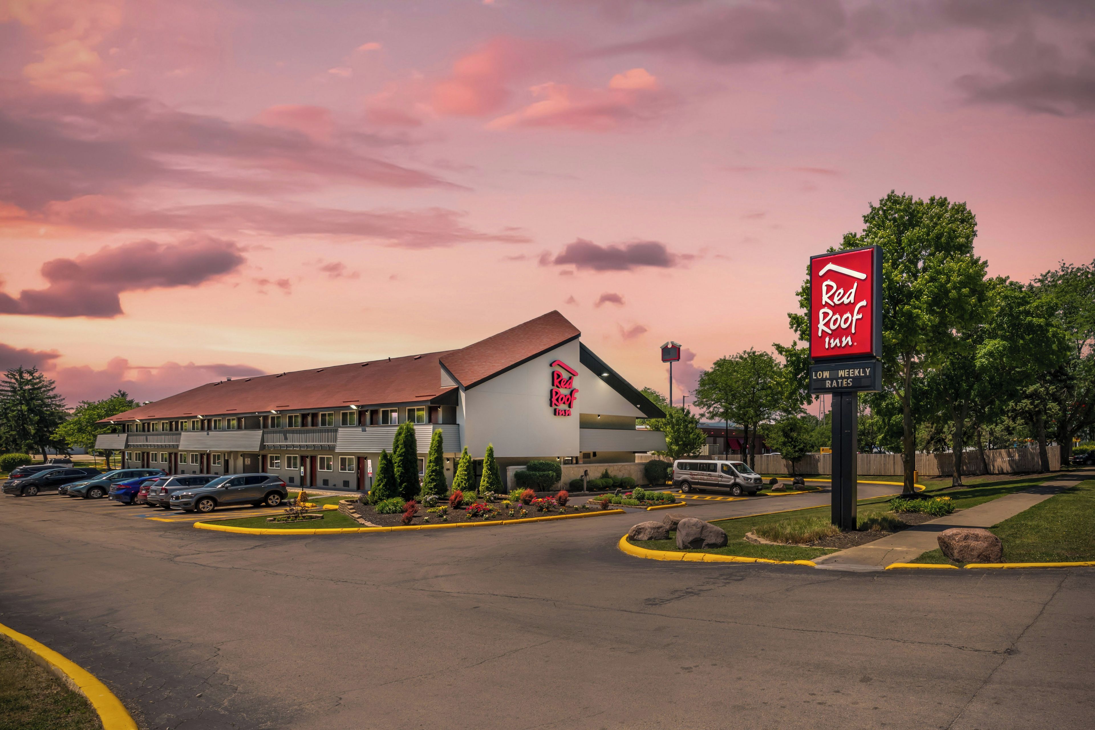 A Red Roof Inn with a parking lot, a building with a red roof, and a sign indicating low weekly rates.