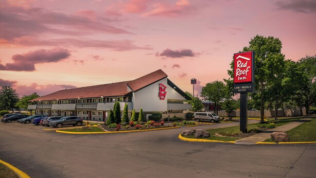 A Red Roof Inn with a parking lot, a building with a red roof, and a sign indicating low weekly rates.