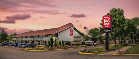 A Red Roof Inn with a parking lot, a building with a red roof, and a sign indicating low weekly rates.