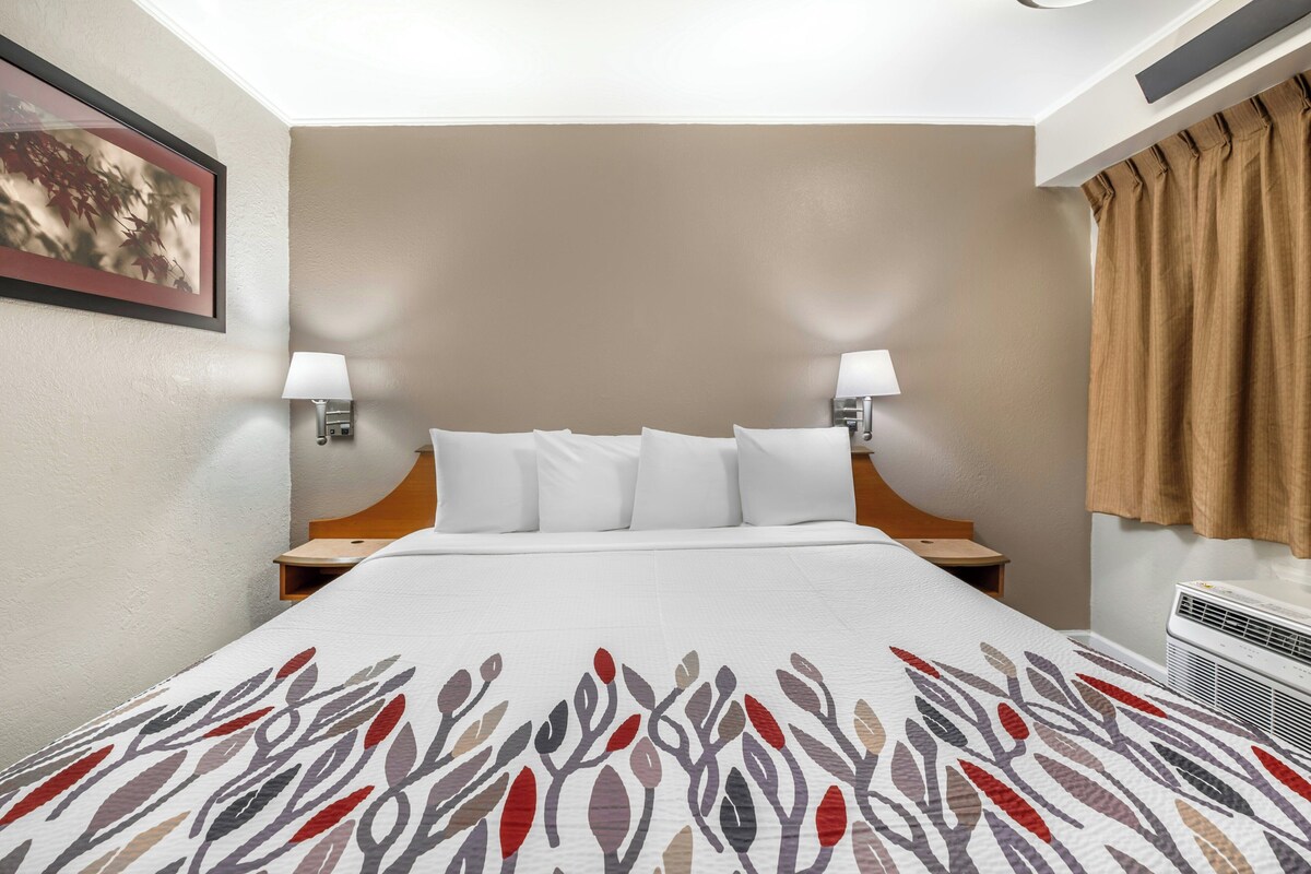 Quarto de hotel com cama, duas luminárias de cabeceira, ar condicionado fixado na parede e um quadro emoldurado.