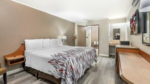 A hotel room with a bed, bedside table, chair, desk, and mirror.