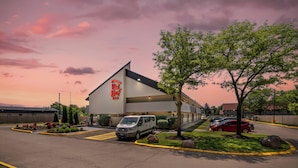 A Red Roof Inn with a parking lot, a van, and a red car parked outside. - Red Roof Inn Chicago - Joliet (Joliet)