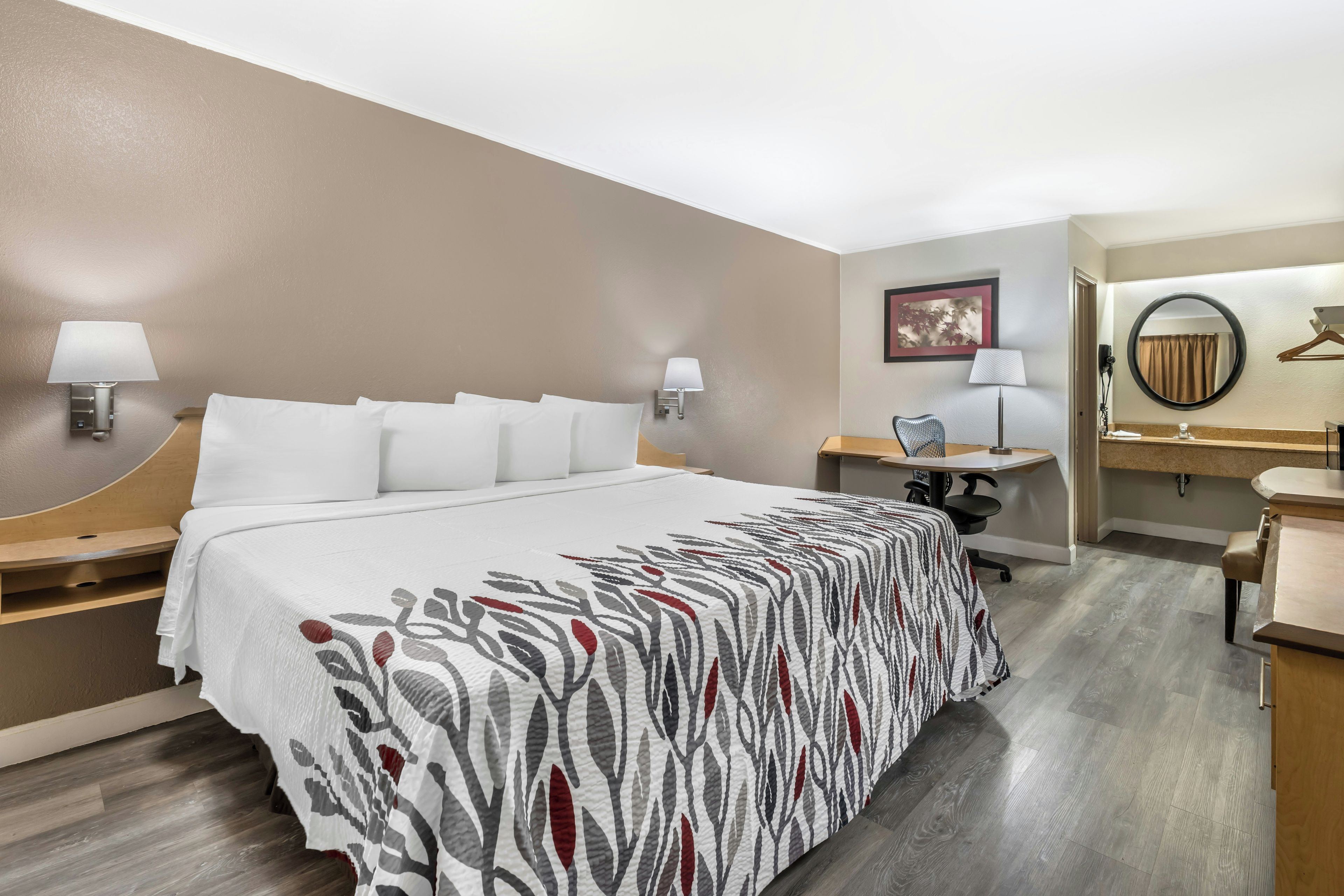Habitación de hotel con cama, mesitas de noche, escritorio, silla, espejo y lámpara de pared.
