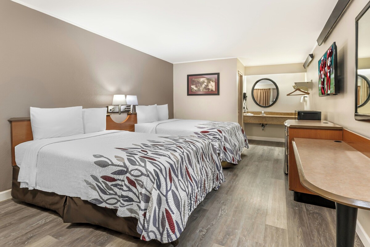 A hotel room with two beds, a desk, a mirror, and a television.
