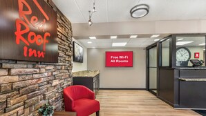 A Red Roof Inn reception area with a stone wall, a red chair, a plant, and a sign indicating free Wi-Fi in all rooms. - Red Roof Inn Chicago - Joliet (Joliet)