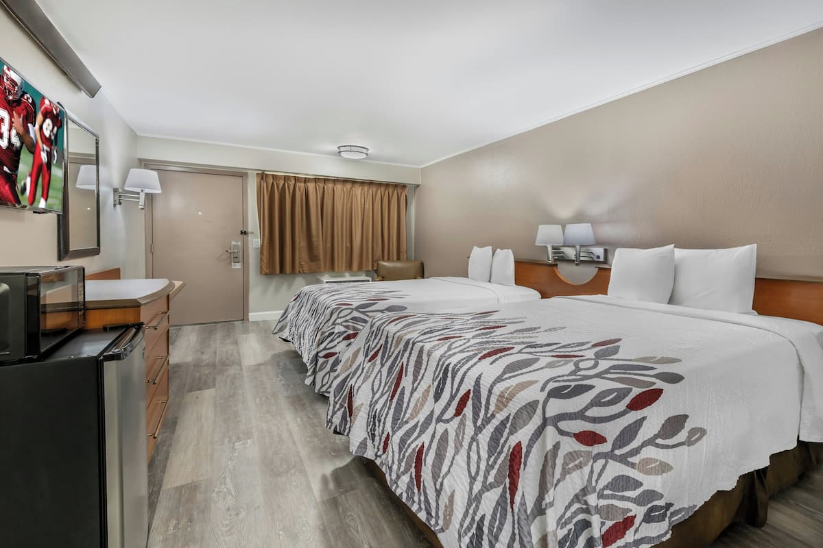 A hotel room with a bed, bedside tables, a desk, a television, and a window with curtains.