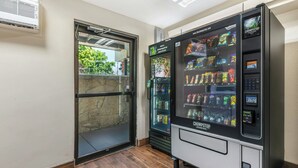 A vending machine with snacks and a water dispenser, a glass door entrance, and a stone wall. - Red Roof Inn Chicago - Joliet (Joliet)