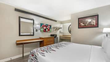 A hotel room with a bed, a desk, a chair, a mirror, a TV, and a bathroom.