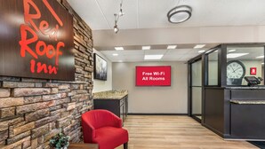 A Red Roof Inn reception area with a stone wall, a red chair, a plant, and a sign indicating free Wi-Fi in all rooms.