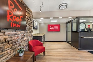 A Red Roof Inn reception area with a stone wall, a red chair, a plant, and a sign indicating free Wi-Fi in all rooms.