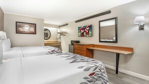 A hotel room with two beds, a desk, a mirror, a TV, and a lamp.