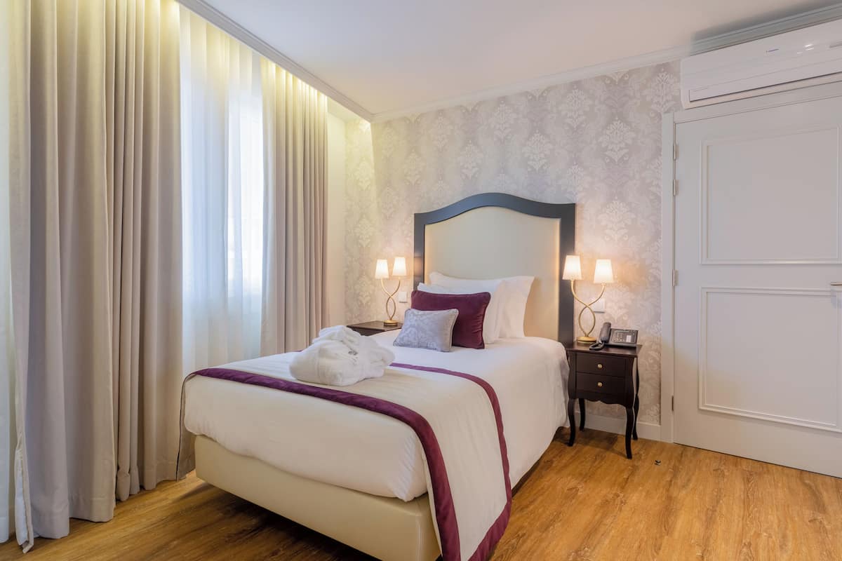 A hotel room with a bed, curtains, a nightstand, and a wall-mounted air conditioner.