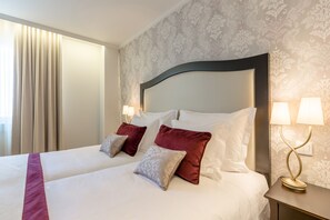Una habitación de hotel con una cama grande, dos lámparas de noche y un papel tapiz estampado.