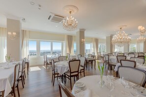 Un comedor amplio con varias mesas y sillas, candelabros elegantes y ventanas grandes que ofrecen vistas a la ciudad.
