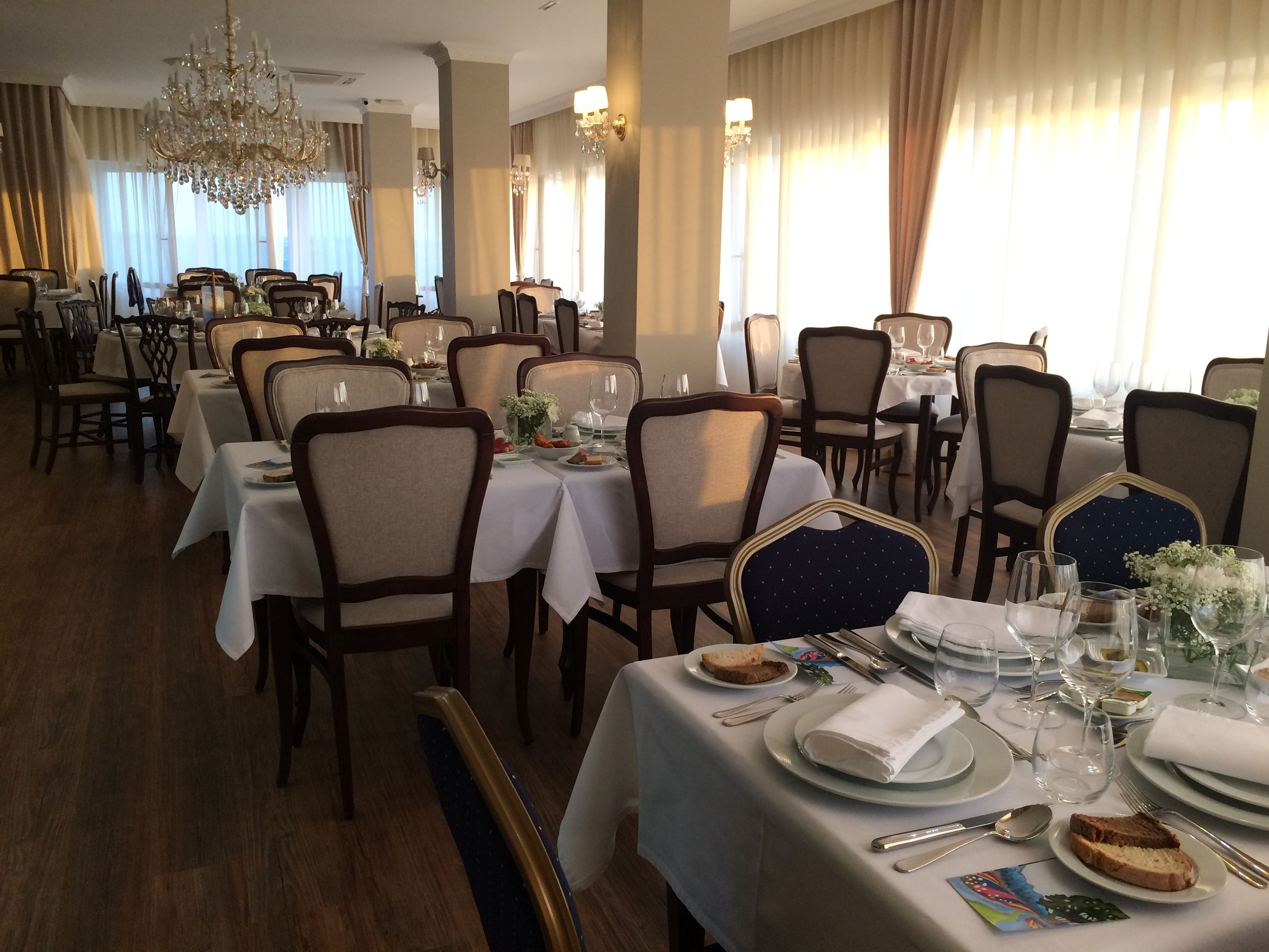 Un comedor formal con varias mesas dispuestas para comidas, sillas elegantes y una araña.