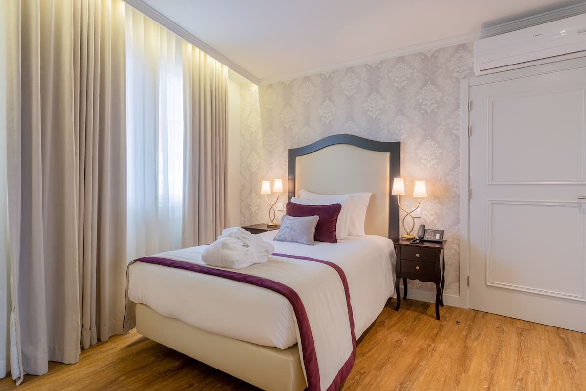Une chambre d’hôtel avec un lit, des rideaux, une table de chevet et un climatiseur fixé au mur.