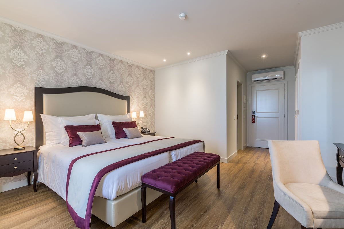 Une chambre à coucher avec un grand lit, un banc, une chaise et une table de chevet avec des lampes.