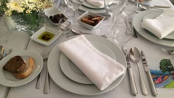 Una mesa dispuesta para una comida, con platos, cubiertos, vasos y un pequeño jarrón con flores.