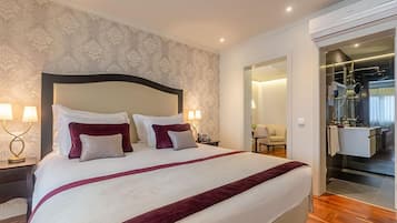 A hotel room with a large bed, two bedside lamps, a nightstand, a mirror, and a bathroom visible through an open door.
