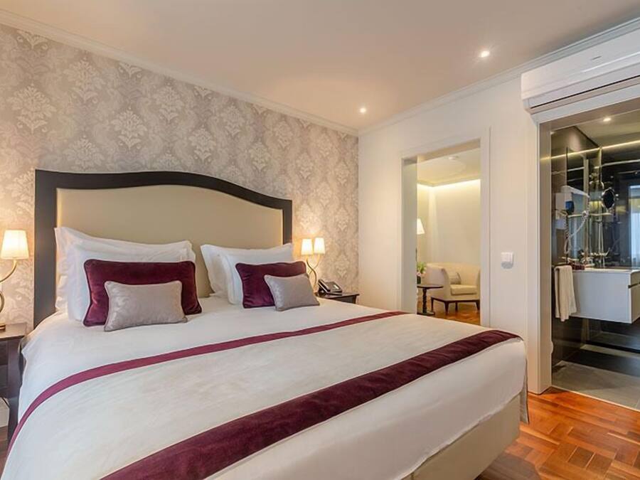 A hotel room with a large bed, two bedside lamps, a nightstand, a mirror, and a bathroom visible through an open door.