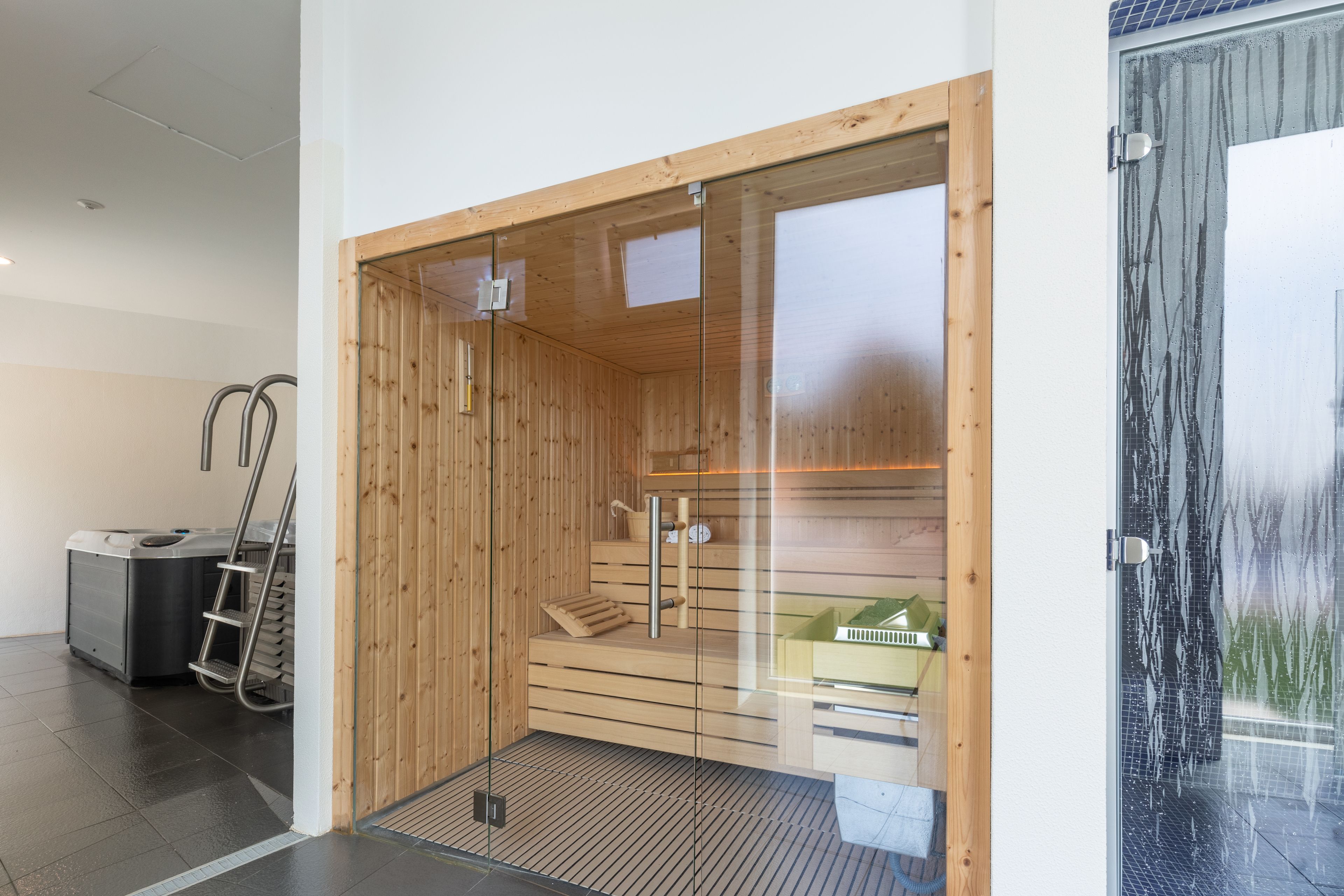 Un cuarto de sauna con paredes de madera, una puerta de vidrio y un banco.