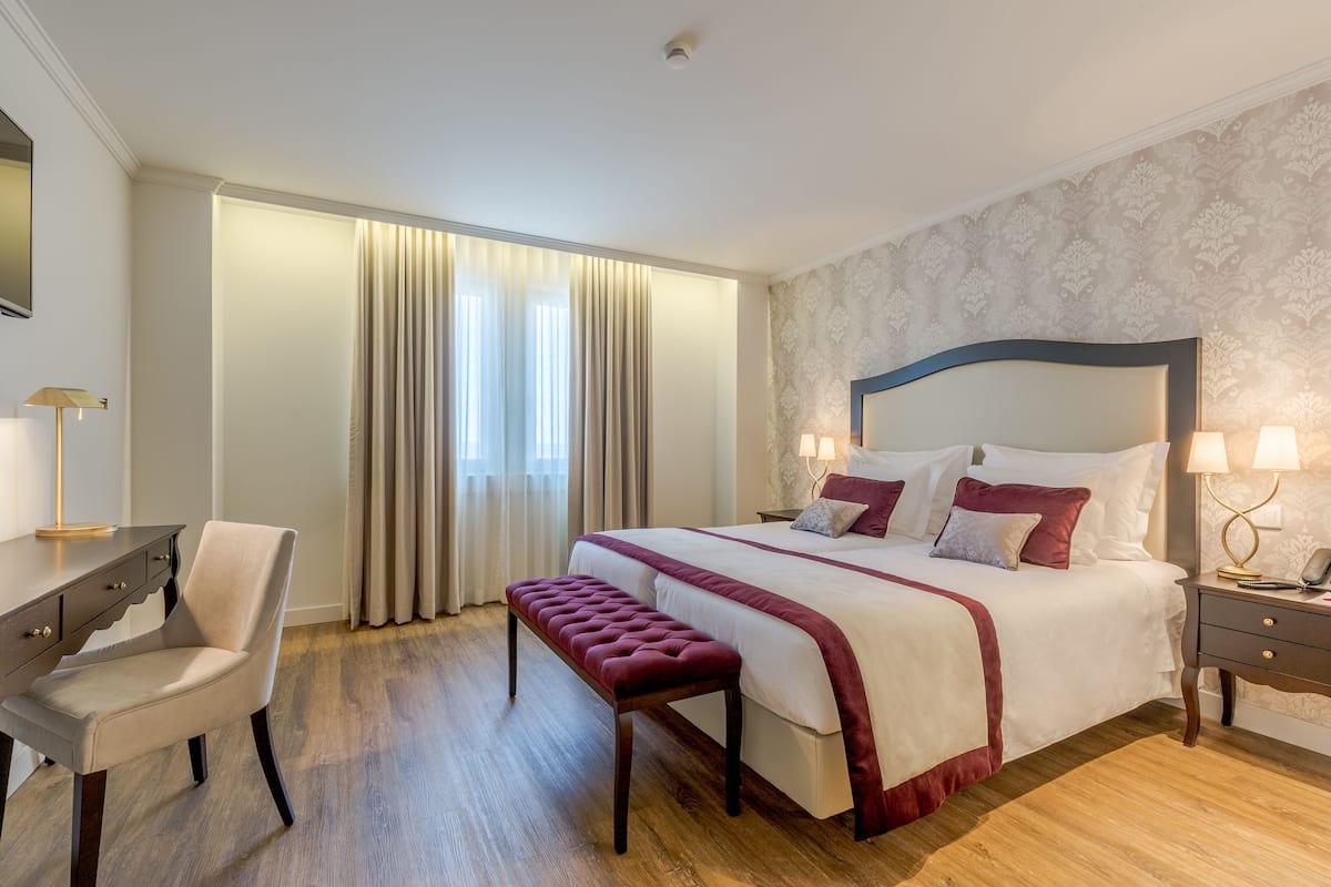 Une chambre d’hôtel comprenant un lit, un bureau, une chaise, un banc, une table de chevet et une lampe.