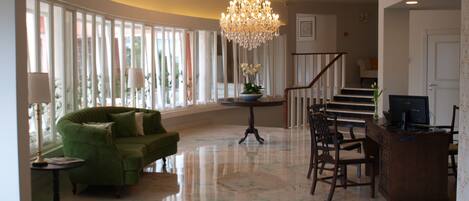 A spacious living room with a green sofa, a chandelier, a dining table with chairs, and a staircase leading to another level.
