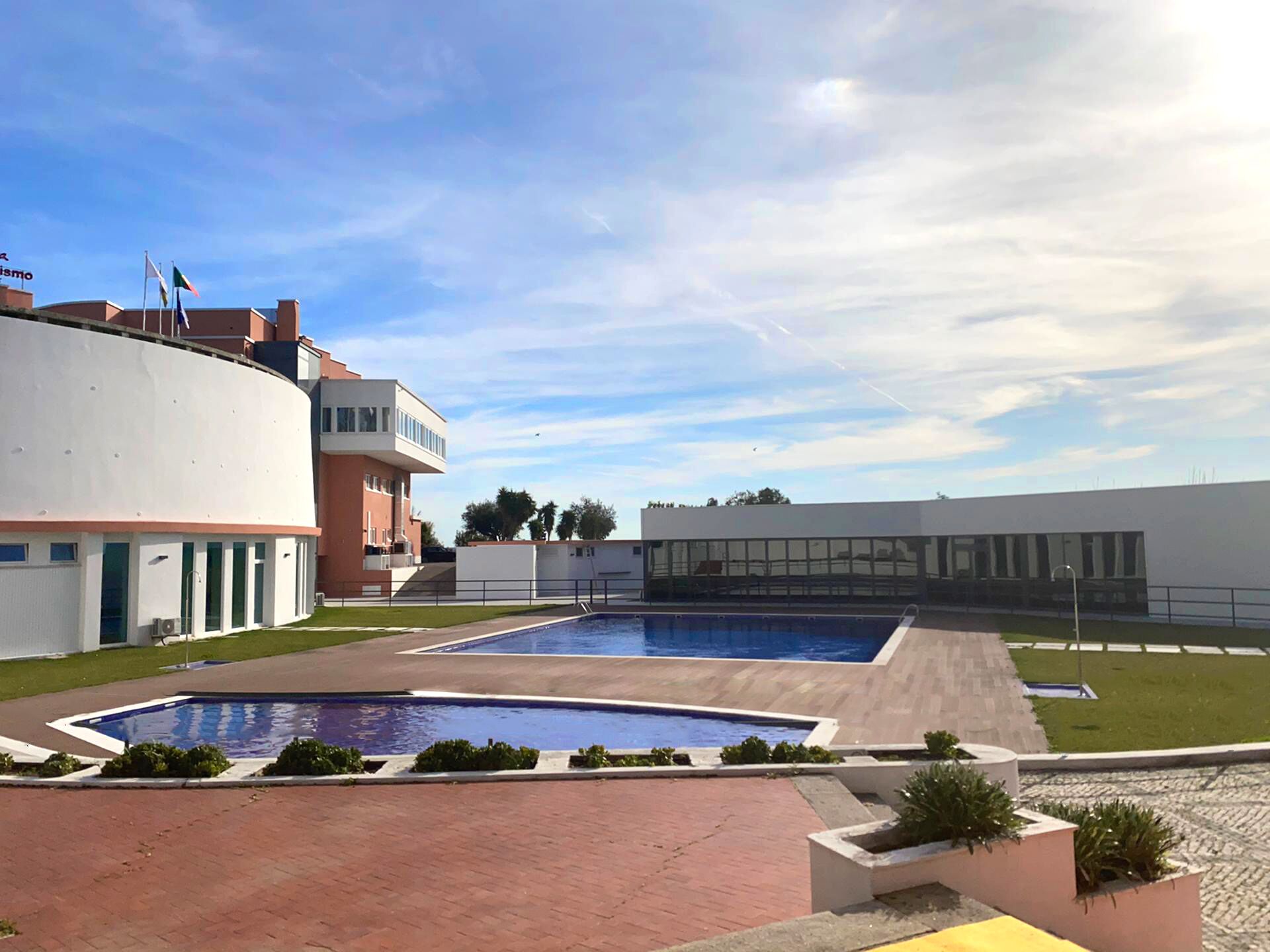 A swimming pool area with modern architecture, including a curved building and a rectangular building with large windows.