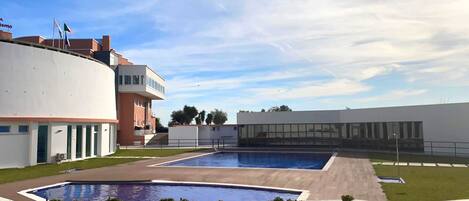 A swimming pool area with modern architecture, including a curved building and a rectangular building with large windows.