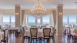 A dining area with a chandelier, tables, chairs, and large windows with a view. - Luna Hotel Turismo (Abrantes)
