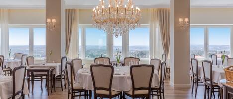 Comedor con candelabro, mesas, sillas y ventanas amplias con vistas.