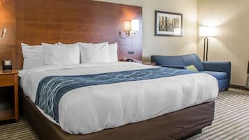 A hotel room with a large bed, a desk, a chair, a lamp, and a framed picture on the wall.
