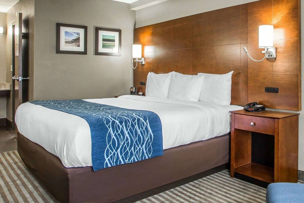 A hotel room with a large bed, a wooden headboard, two wall-mounted lamps, a bedside table with a phone, and a small drawer.
