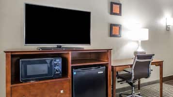 A hotel room with a flat-screen TV, a microwave, a mini-fridge, a desk, a chair, and a lamp.