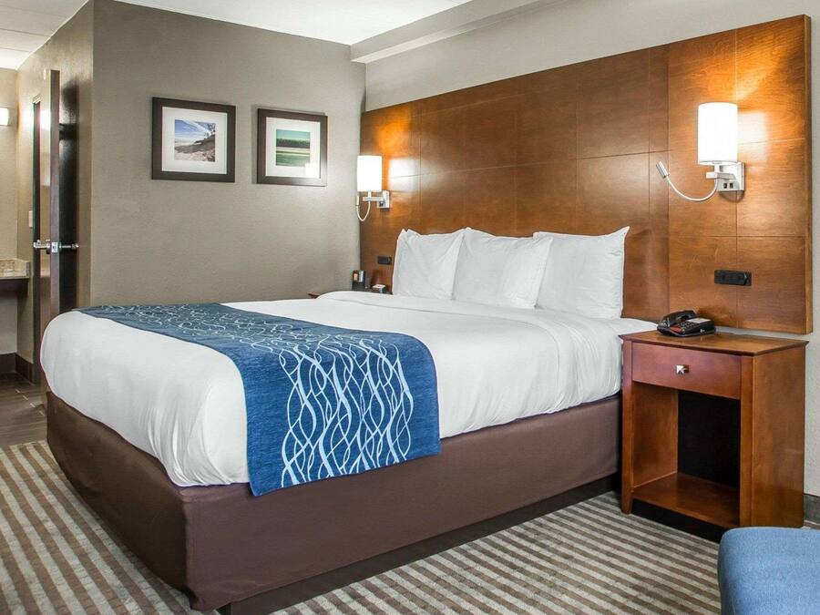 A hotel room with a large bed, a wooden headboard, two wall-mounted lamps, a bedside table with a phone, and a small drawer.