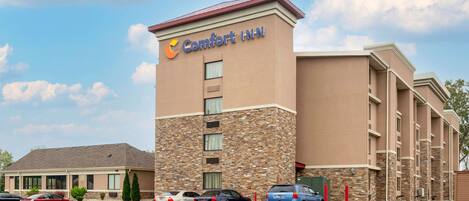 Un hotel Comfort Inn con fachada de ladrillo, varios espacios de estacionamiento y un cielo despejado.