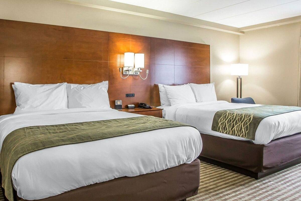 A hotel room with two beds, a wooden headboard, bedside lamps, a telephone, and a patterned carpet.
