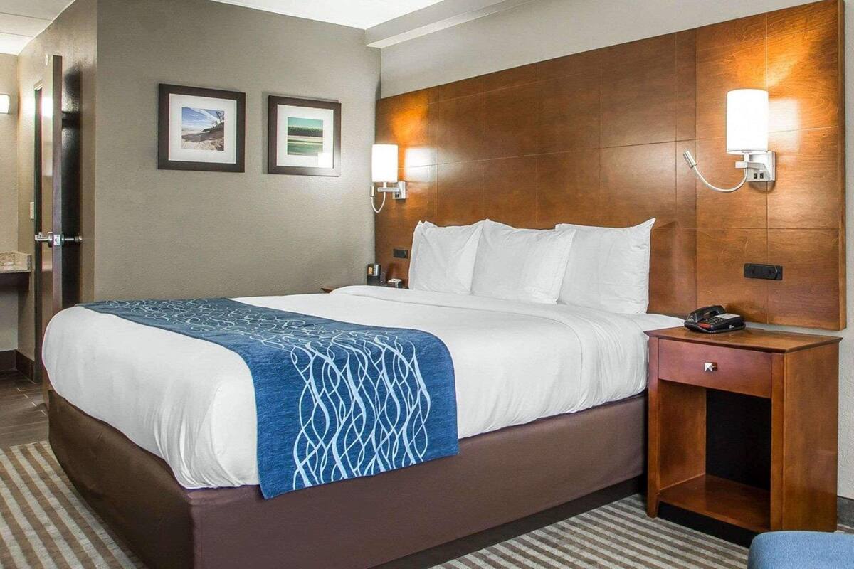 A hotel room with a large bed, a wooden headboard, two wall-mounted lamps, a bedside table with a phone, and a small drawer.