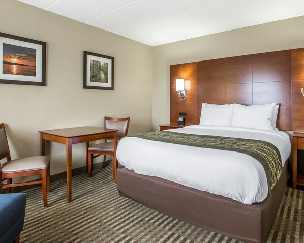 Habitación de hotel con una cama grande, un escritorio, una silla y dos cuadros en la pared.