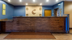 A reception desk with a wooden finish, a large wall clock, and a reception area with a blue wall and a wooden floor. - Comfort Inn Hammond I-94 (Hammond)