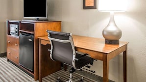 A hotel room with a wooden desk, a black office chair, a television on a cabinet, and a wall-mounted lamp. - Comfort Inn Hammond I-94 (Hammond)