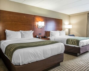 A hotel room with two beds, a wooden headboard, bedside lamps, and a check-in counter.
