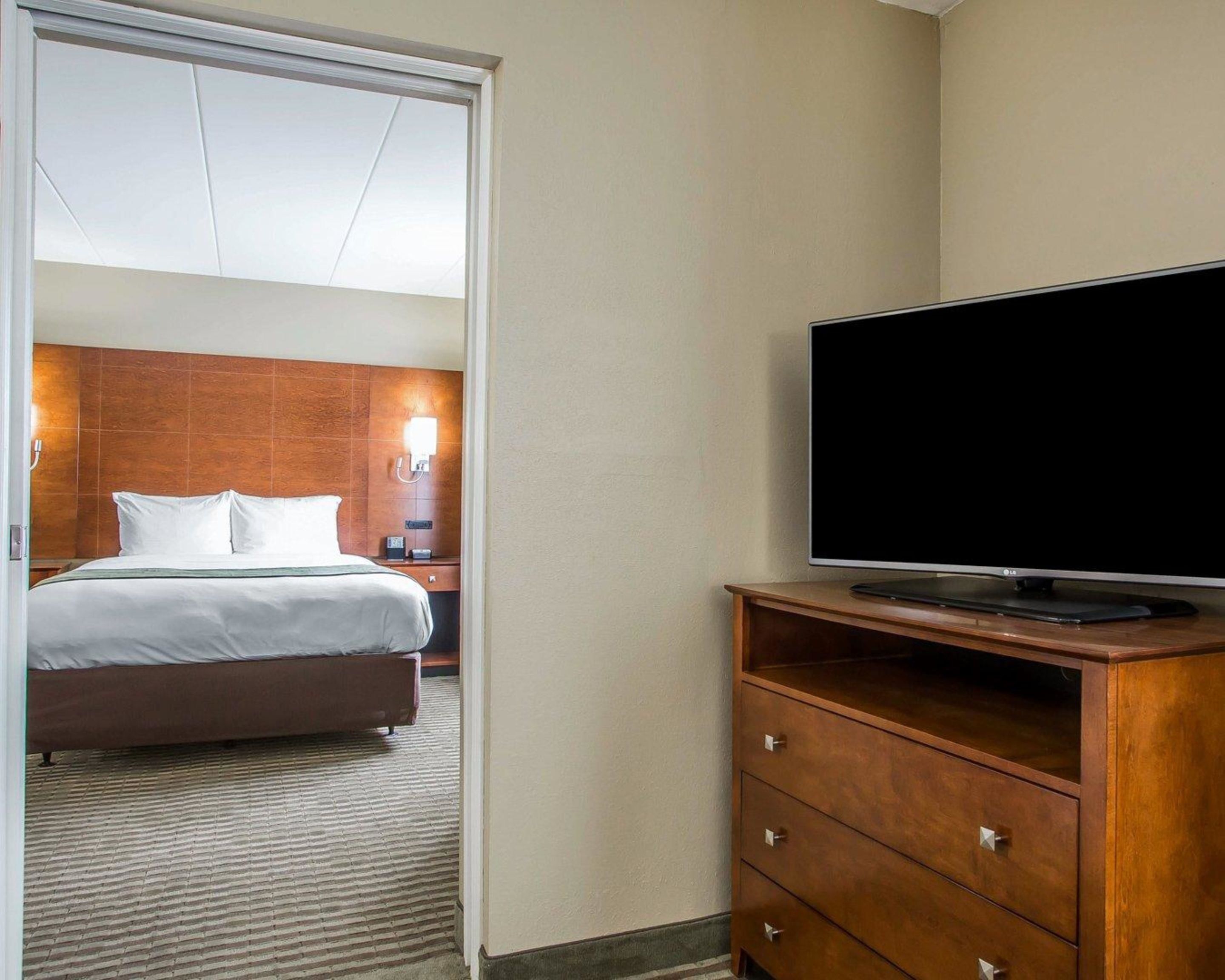 Una habitación de hotel con una cama, un televisor sobre un soporte de madera y una puerta que da a otra habitación.