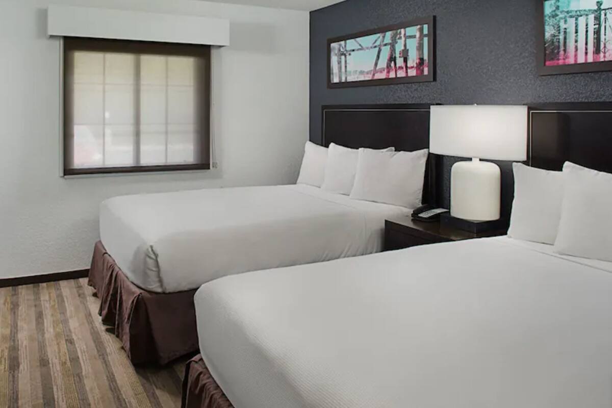 Une chambre d’hôtel avec deux lits, une fenêtre, un téléviseur et des œuvres d’art accrochées au mur.