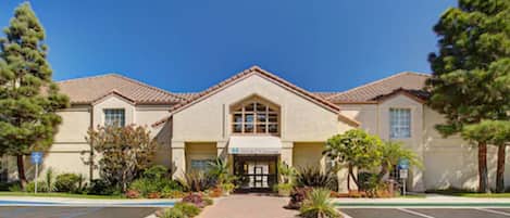 A hotel with a central entrance, a parking lot, and landscaped gardens.
