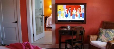 A hotel room with a bed, a television mounted on the wall, a chair, and a small table with a cup and saucer.